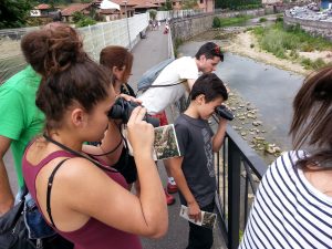 A group of people observe birds with their binoculars, next to the river Sella.