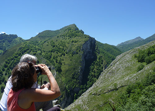 Una pareja esta sentada mirando con unos prismáticos hacia el paisaje de montañas